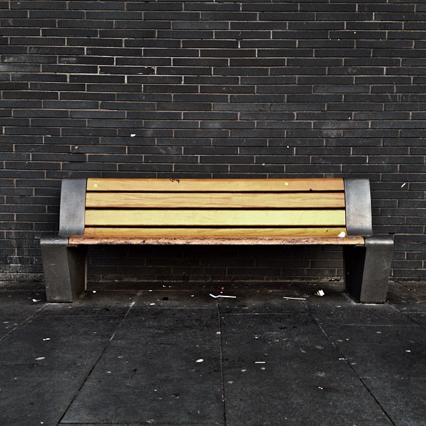 An empty wooden bench against a slate wall