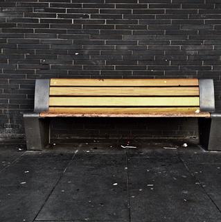 An empty wooden bench against a slate wall