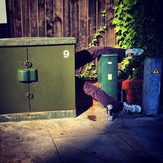 A pair of legs sticking out from behind an electricity cabinet with a can of beer on the floor