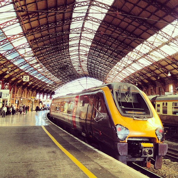 A yellow and purple train waiting at a station underneath a steel canompy