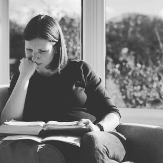 A woman sat reading a bible in a bay window