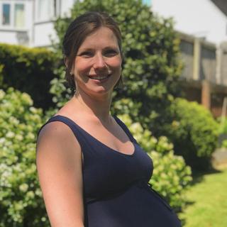 A pregnant woman standing holding her belly in a garden. 