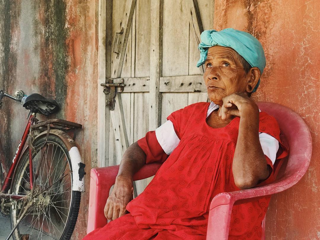 A blind woman sat down in a chair wearing a green headscarf and red dress