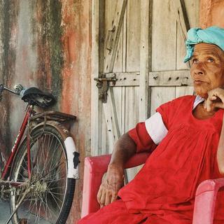 A blind woman sat down in a chair wearing a green headscarf and red dress