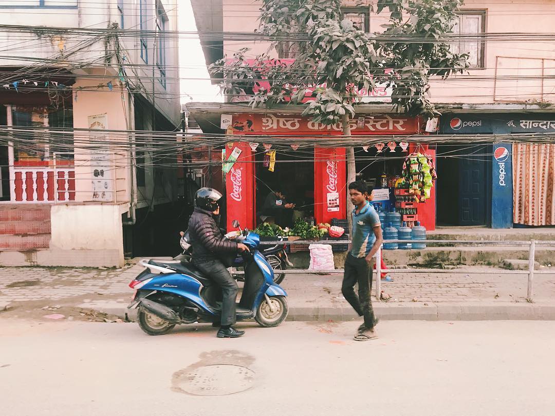 A man on a motorbike and a man walking in front of a nepalese shop front