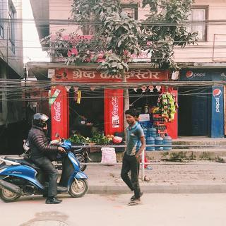 A man on a motorbike and a man walking in front of a nepalese shop front