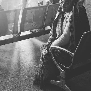 An old woman sitting in an airport chair in black and white