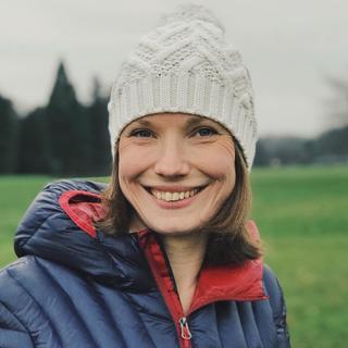 A woman smiling wearing a white bobble hat and a blue and red down jacket