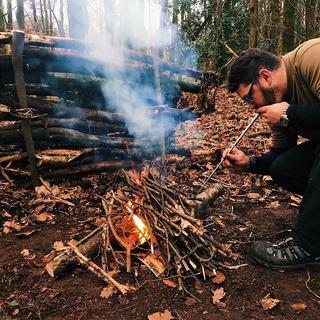 A man blowing air through a pocket bellows into a campfire