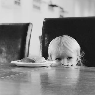 A little girls head at eye level of a table looking at the camera.