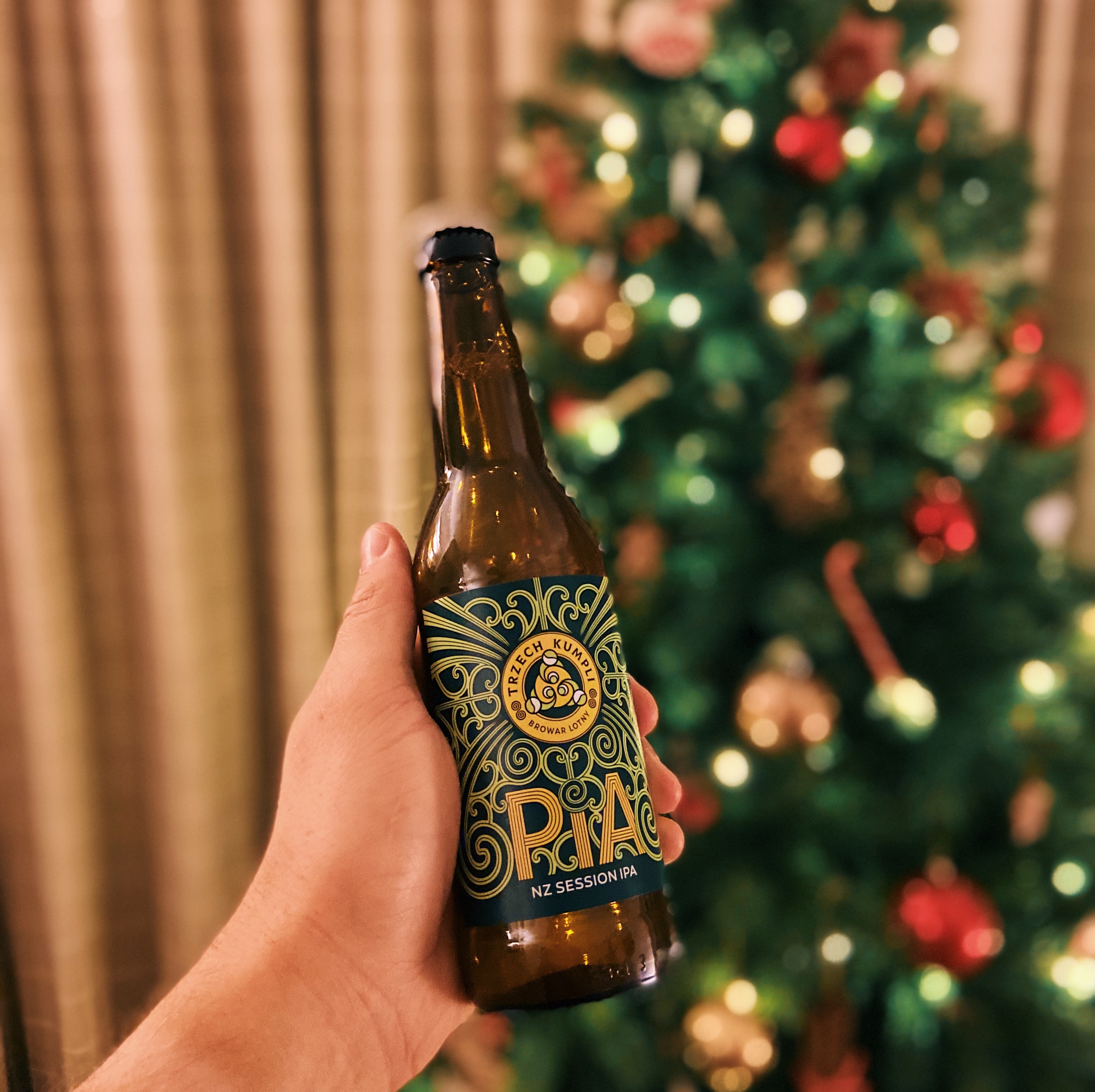 Someone holding a bottle of beer in front of a Christmas tree