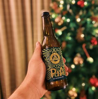Someone holding a bottle of beer in front of a Christmas tree