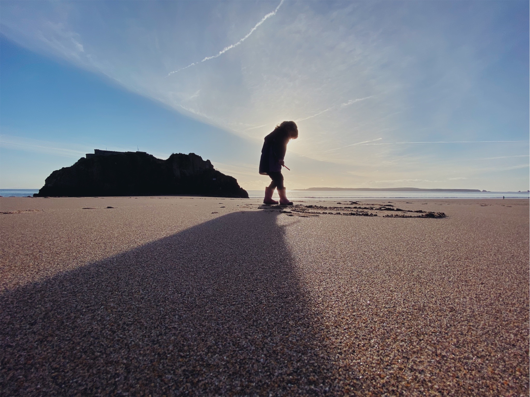 A little girl playing on the beach in silhouette with Caldey island in the background