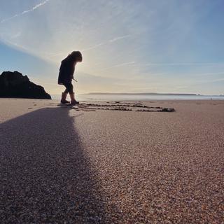 A little girl playing on the beach in silhouette with Caldey island in the background
