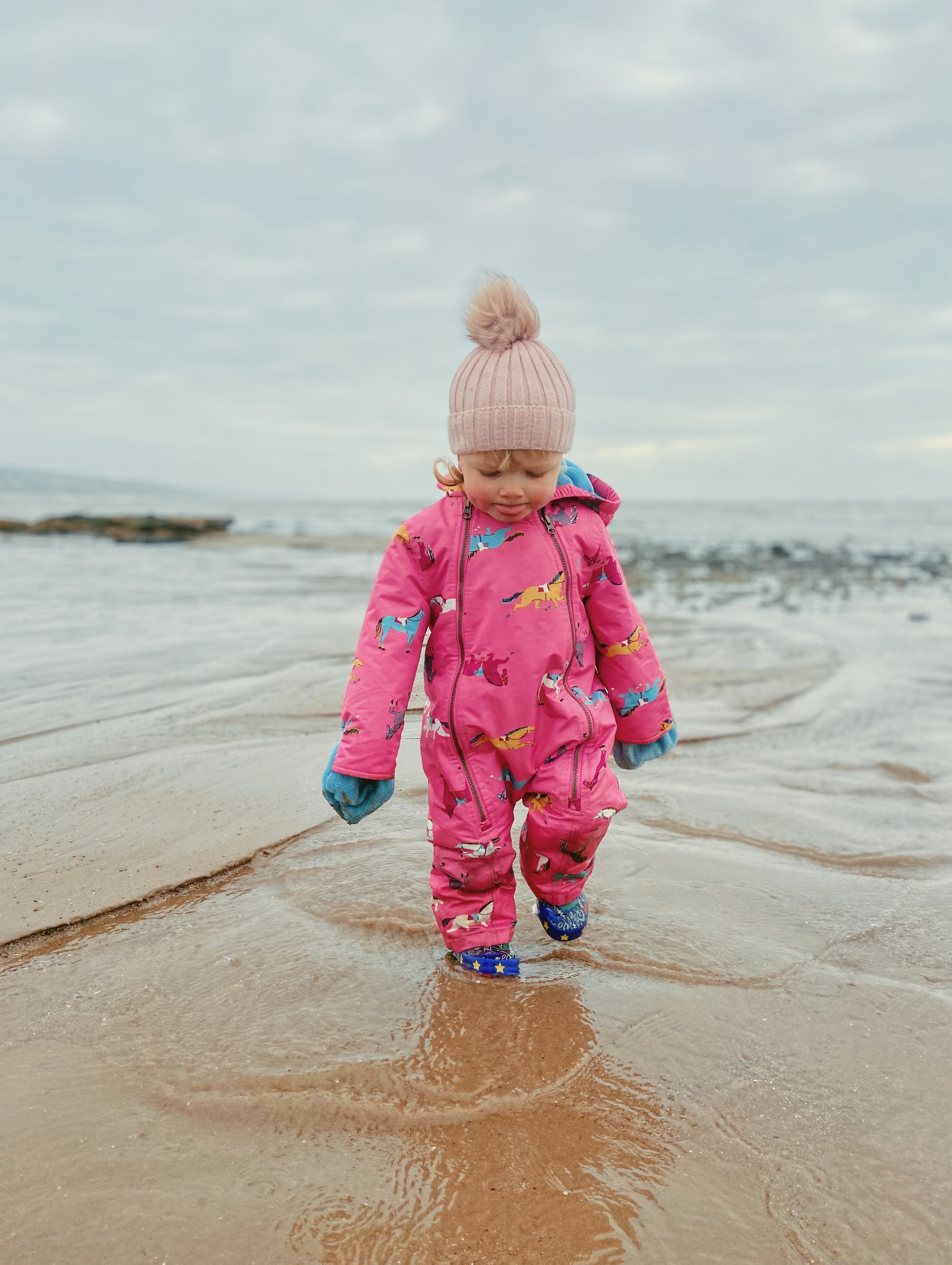 A little girl walking through the water on the beach wearing an all in one