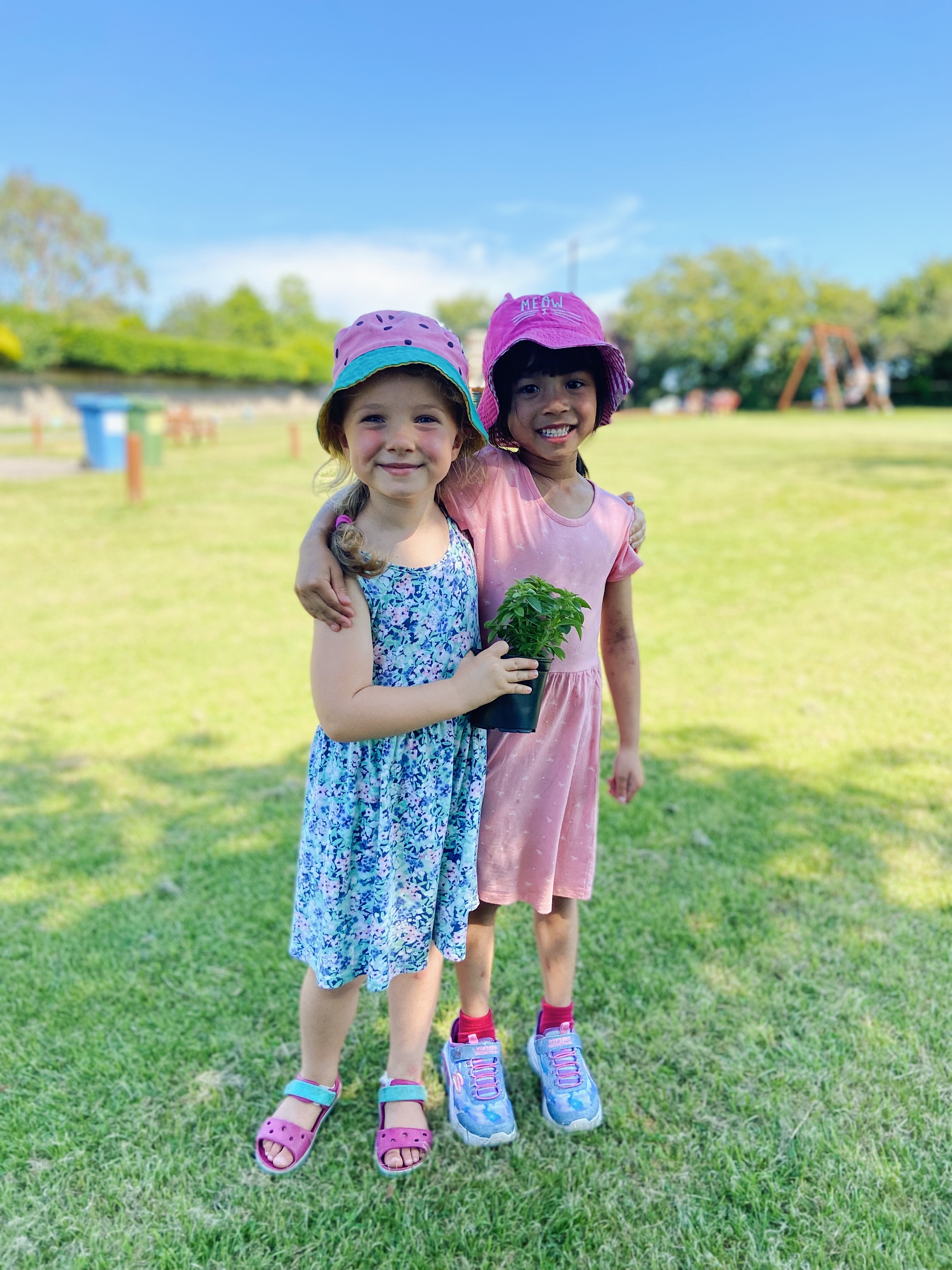 Two girls in summer dresses and hats, hugging whilst looking at the camera