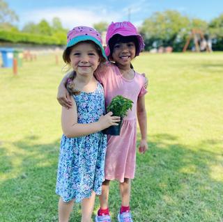 Two girls in summer dresses and hats, hugging whilst looking at the camera